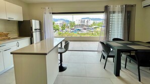 A modern kitchen with a refrigerator, a dining area with a table and chairs, and a view of a cityscape through large windows.