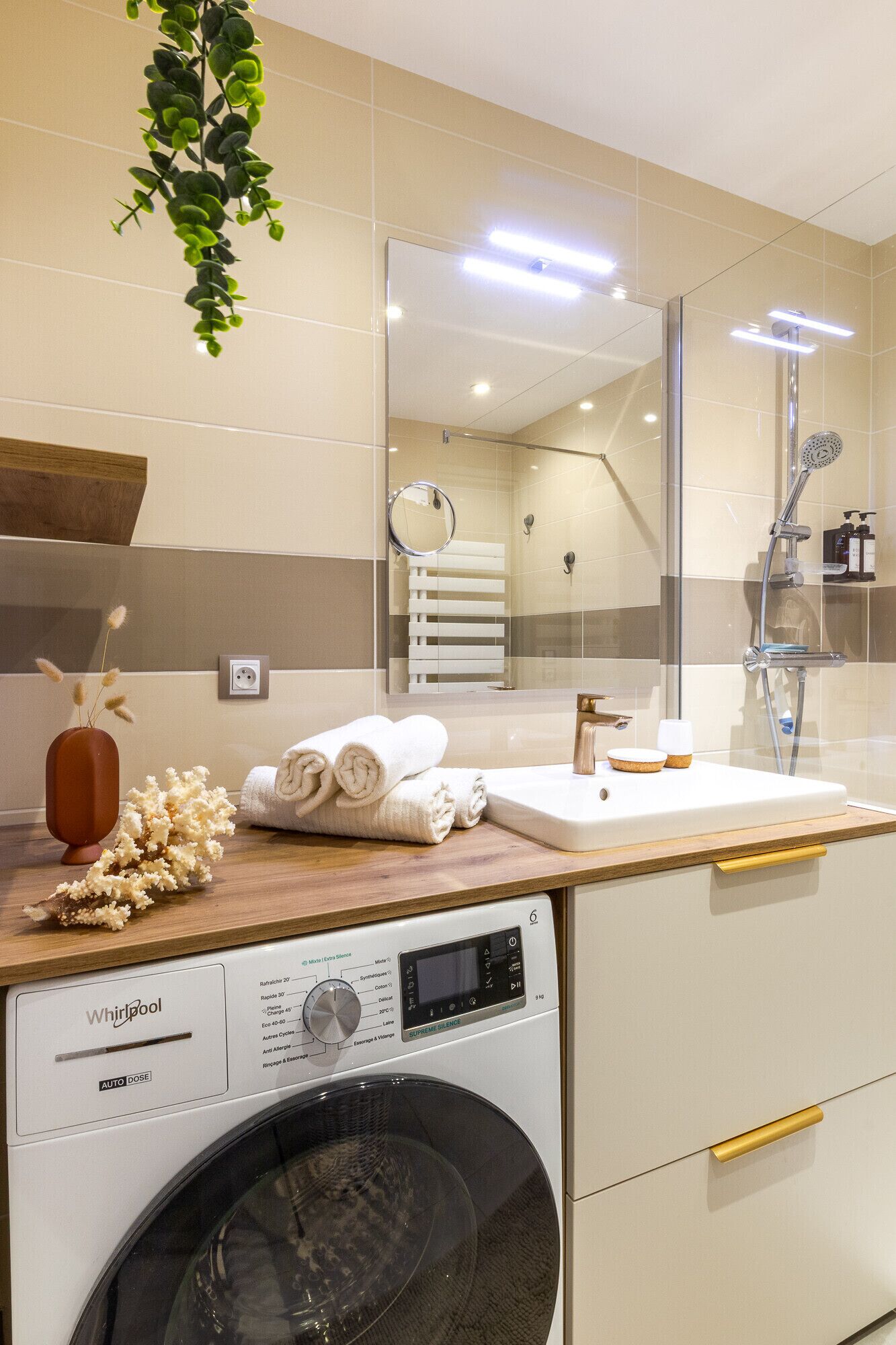 A modern bathroom with a Whirlpool washing machine, a sink, and a shower.