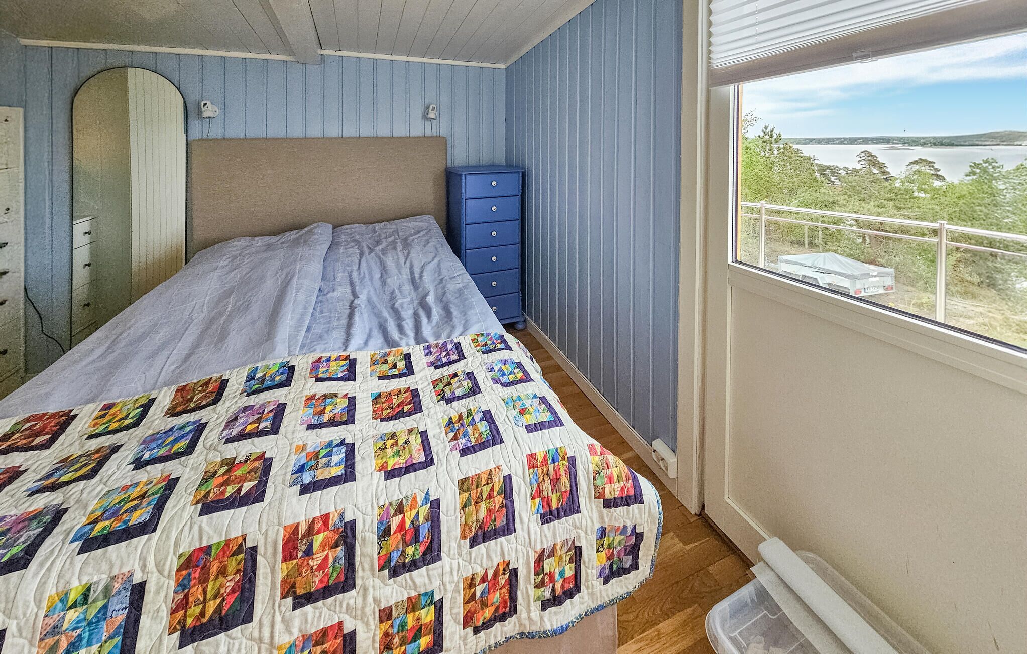 Een slaapkamer met een bed, een dressoir en een raam met uitzicht op een wateroppervlak.