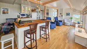 Une cuisine spacieuse avec un îlot central en bois, des tabourets de bar et un coin repas avec des chaises bleues.