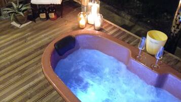 Un jacuzzi con velas y botellas, una terraza de madera y una pequeña mesa con toallas.