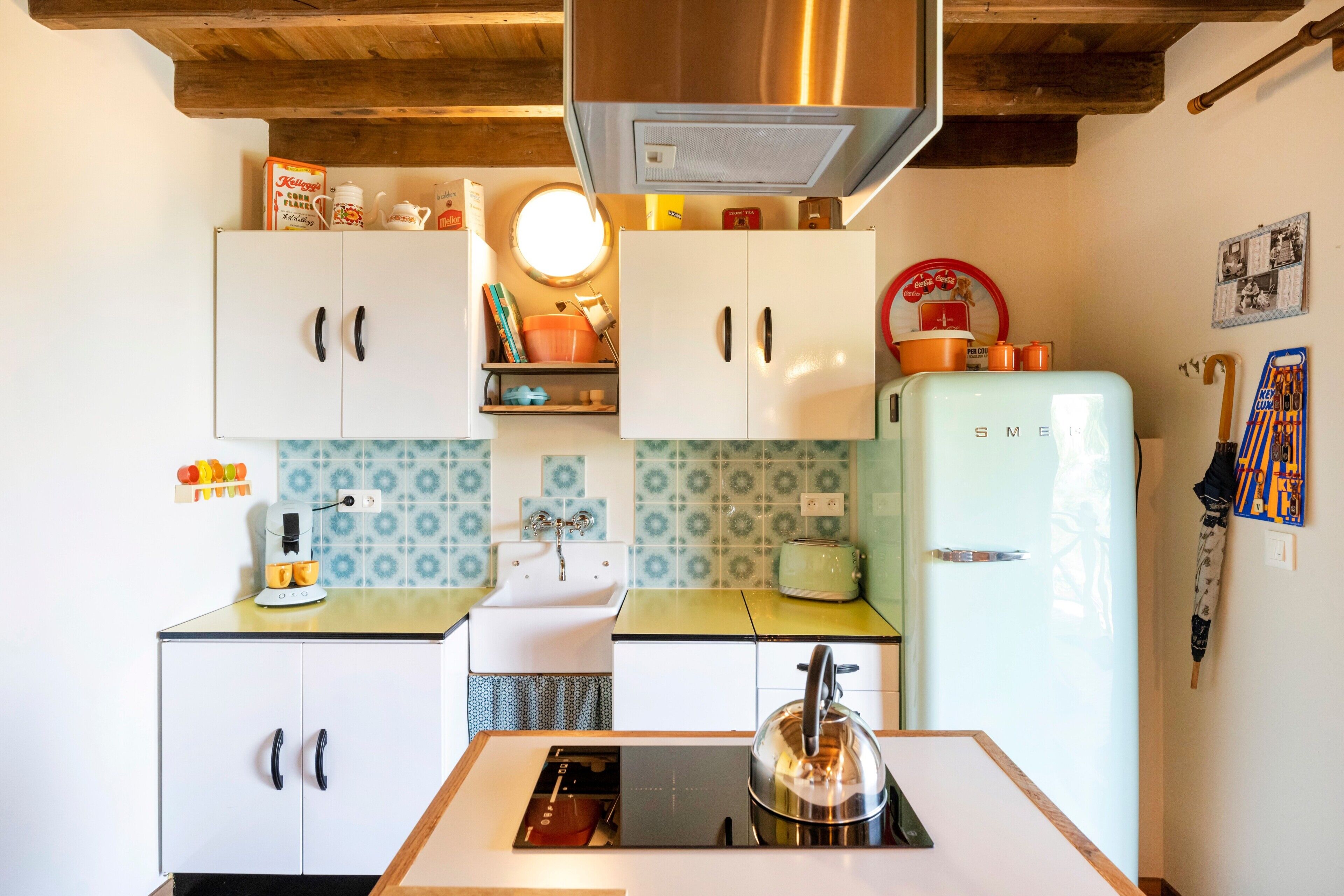 A compact kitchen with white cabinets, a stainless steel range hood, a vintage-style refrigerator, and a small sink.