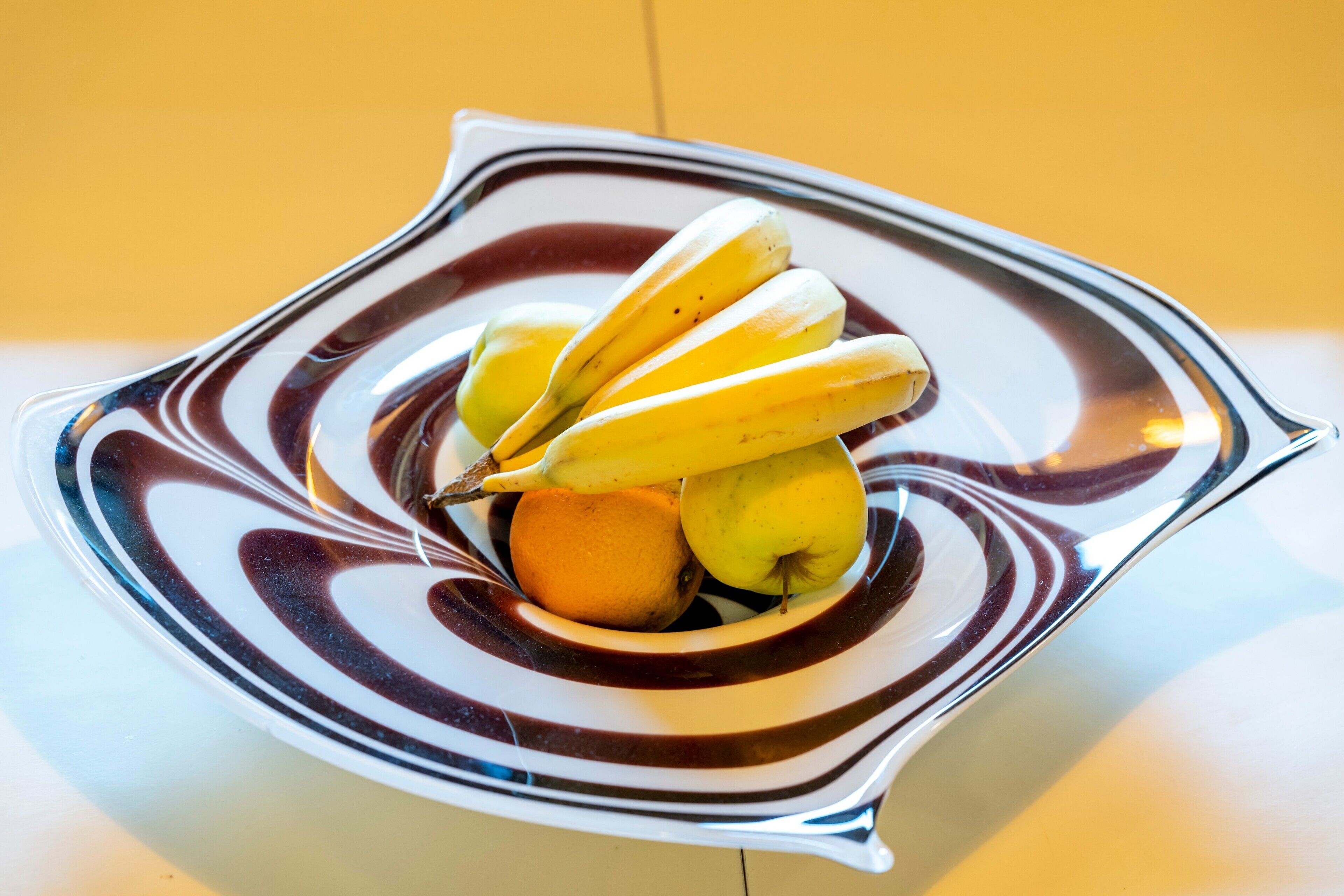 Ein Teller mit Bananen, einem Apfel und einer Orange.