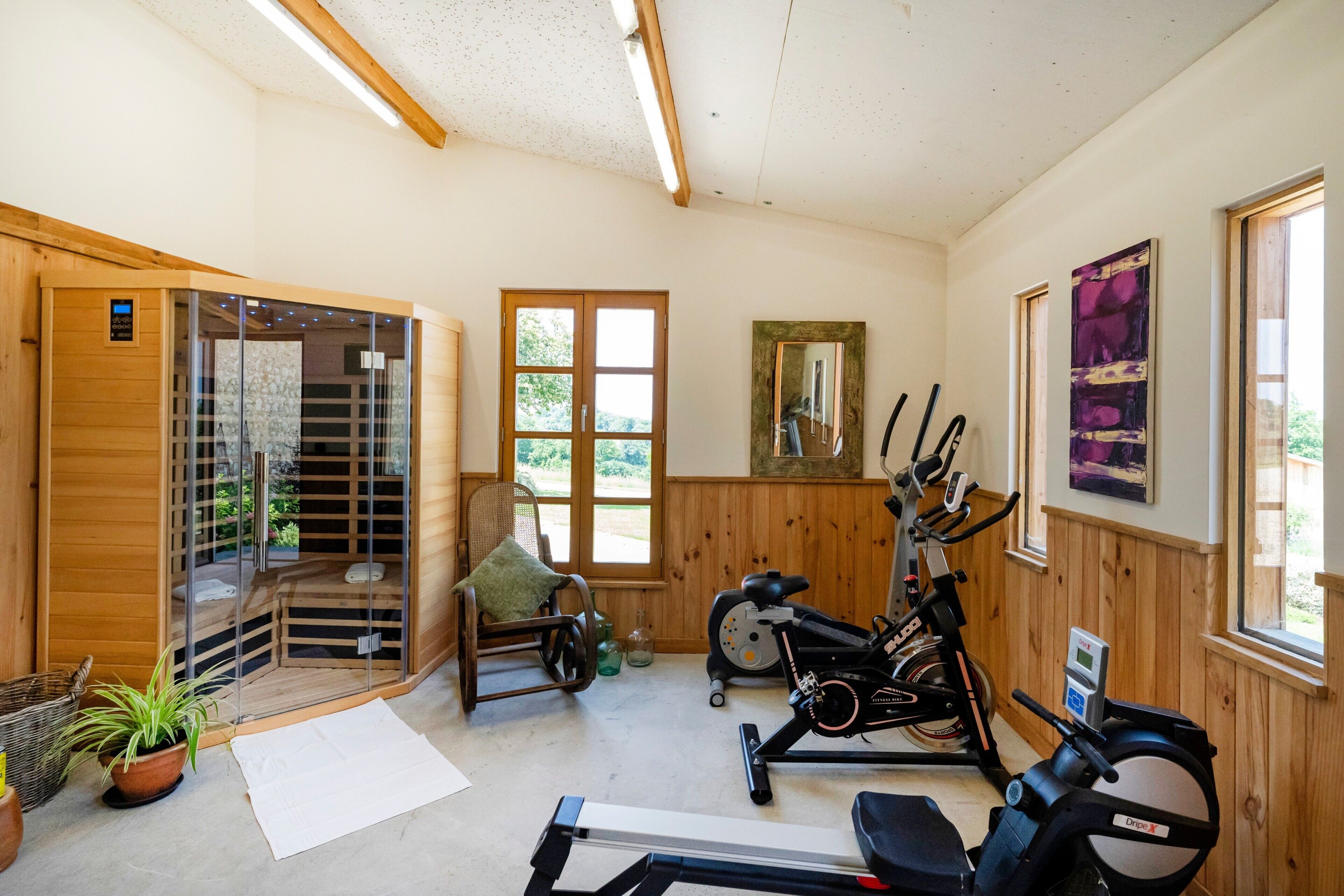 Una habitación con sauna, equipo de ejercicio, una silla y una ventana.