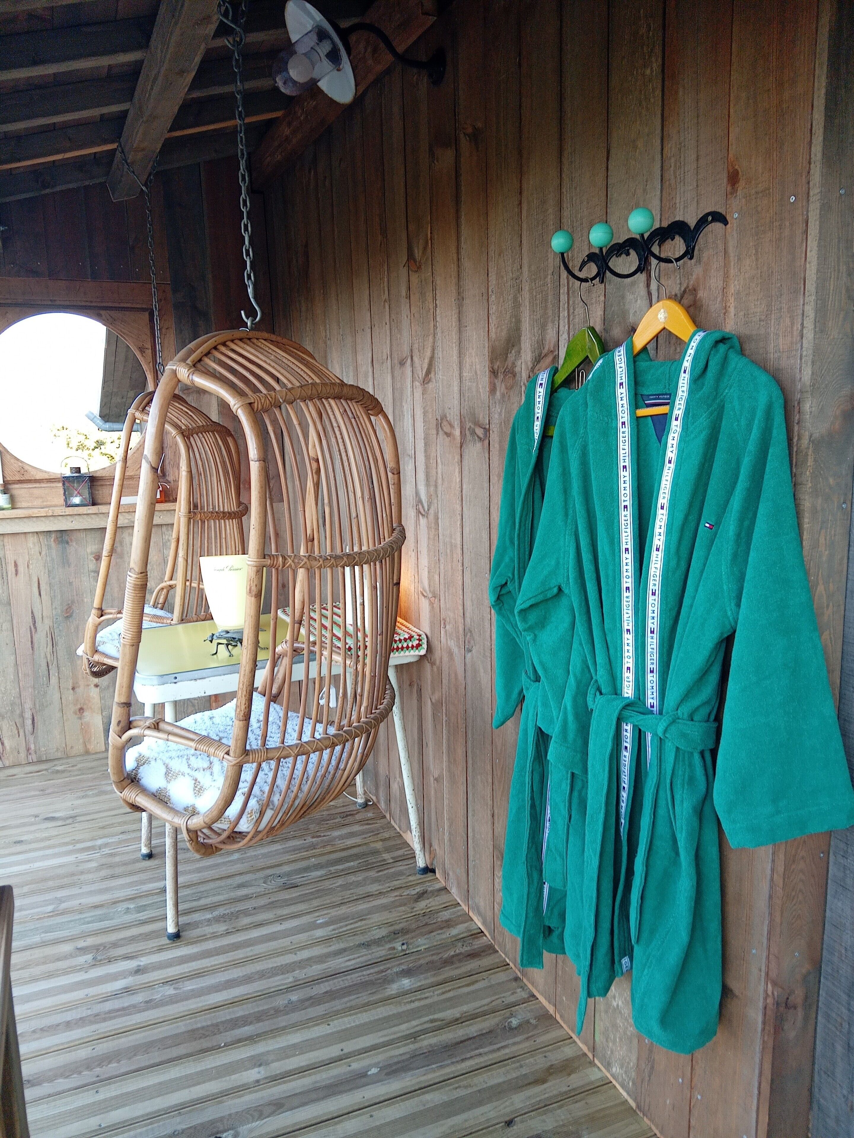 A wicker chair with a cushion, a green robe hanging on a hook, and a wooden floor.