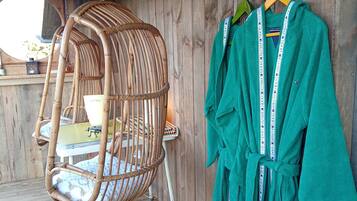 A wicker chair with a cushion, a green robe hanging on a hook, and a wooden floor.