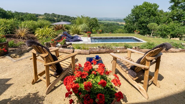 A poolside area with wooden chairs, a small table, and a view of a pool and landscape. - L'Atelier de Scarlett – An Intimate Luxury Escape in the Heart of Gascony (Unknown)