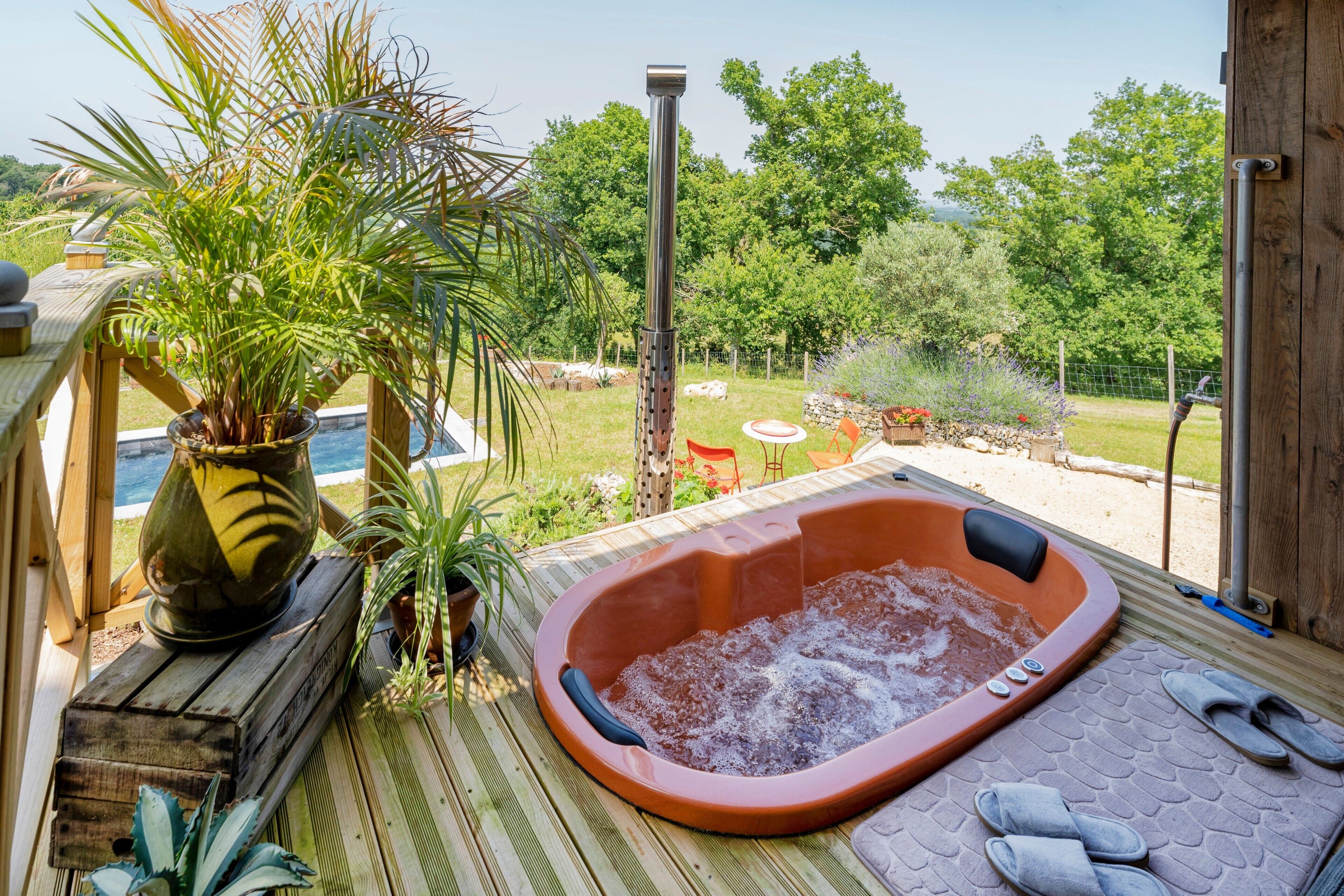Un bain à remous sur une terrasse en bois, avec vue sur une piscine et un jardin.