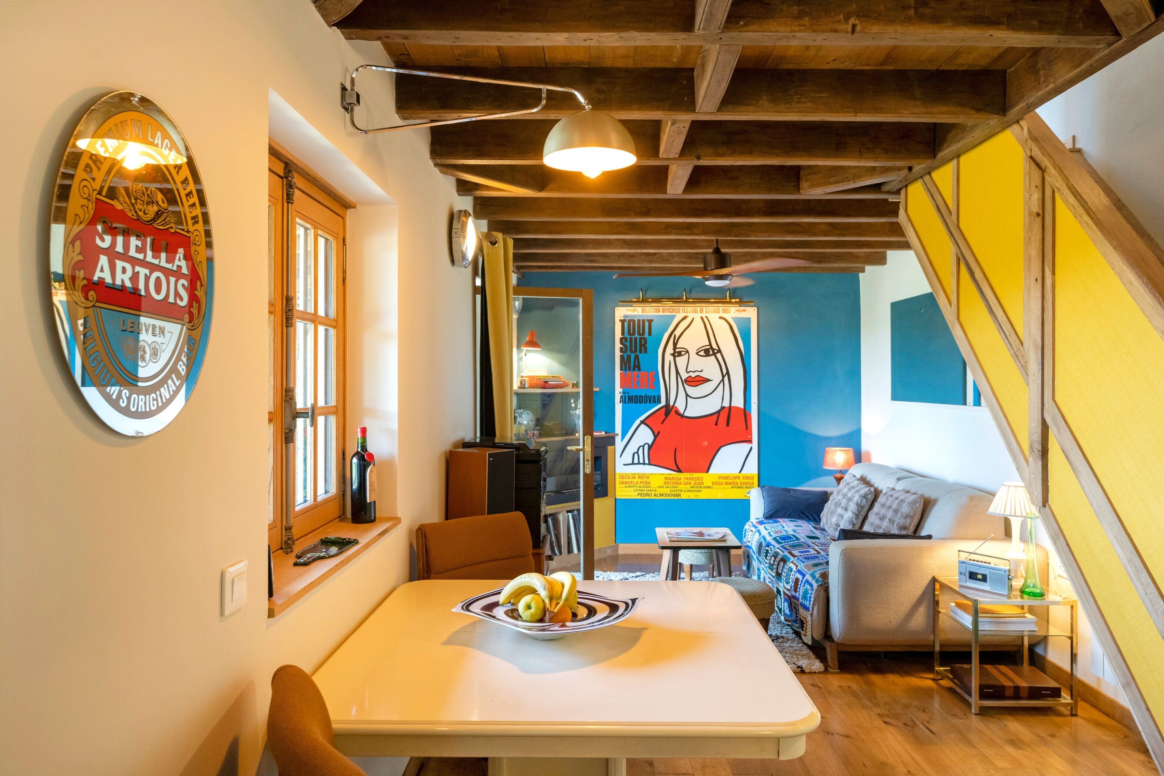 Una habitación con una mesa de comedor, un sofá, una cama, una escalera y una pared con un cartel.