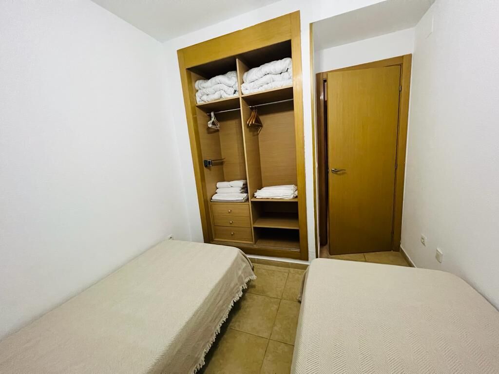 Une petite pièce avec deux lits simples, une armoire en bois avec des étagères et une porte.