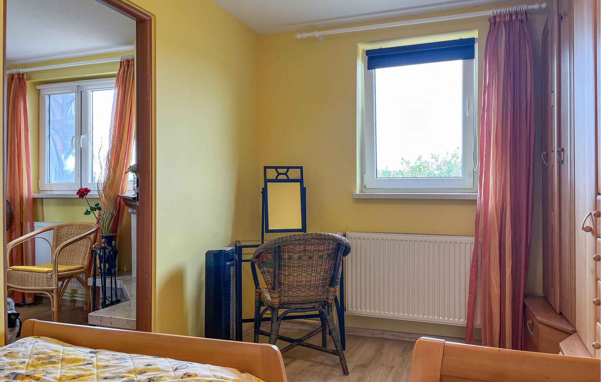 Une pièce comprenant un lit, une chaise, un radiateur et une fenêtre avec des rideaux.