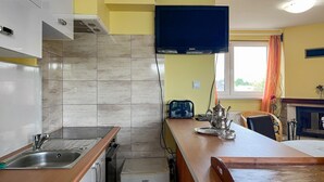 A kitchen with a microwave, toaster, and kettle on the counter, a sink, and a window with curtains.