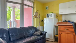 A living room with a black leather sofa, a white refrigerator, a microwave, and a wooden cabinet.
