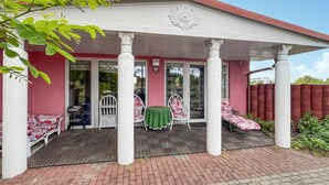 A covered patio with two white chairs and a table, a red fence, and a brick pathway.