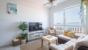 A modern living room with a television, sofa, and a large window offering a view. - Apartment in Cabo Cruz with Sea Views (Unknown)