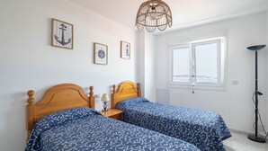 A bedroom with two wooden beds, a hanging light fixture, framed pictures on the wall, and a window. - Apartment in Cabo Cruz with Sea Views (Unknown)