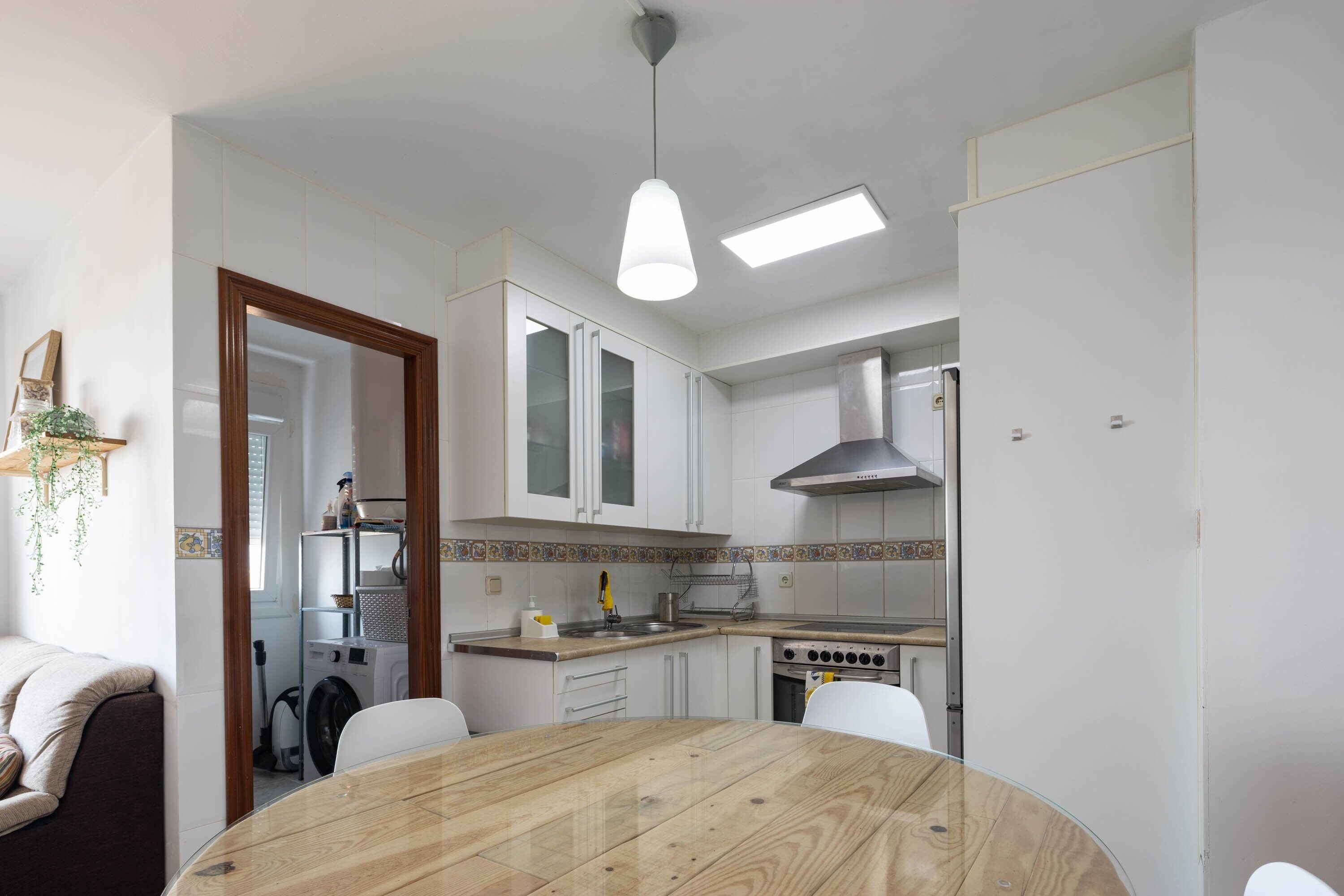 A modern kitchen with white cabinets, a wooden dining table, and a built-in oven.