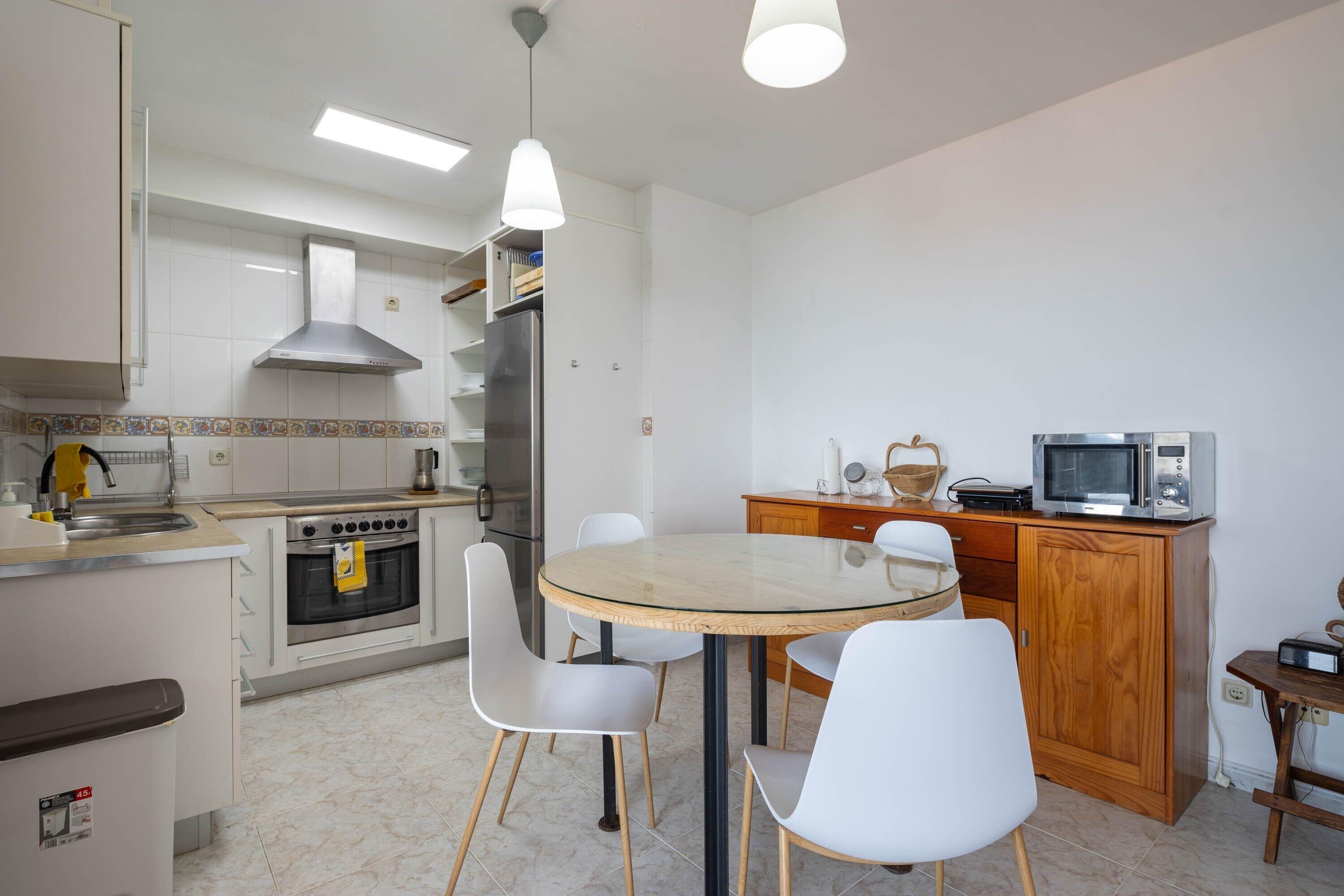 A kitchen with white cabinets, a stainless steel stove, a microwave, and a round glass table with white chairs.