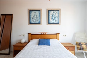 A bedroom with a wooden bed, a nightstand, a chair, and two framed artworks on the wall. - Apartment in Cabo Cruz with Sea Views (Unknown)