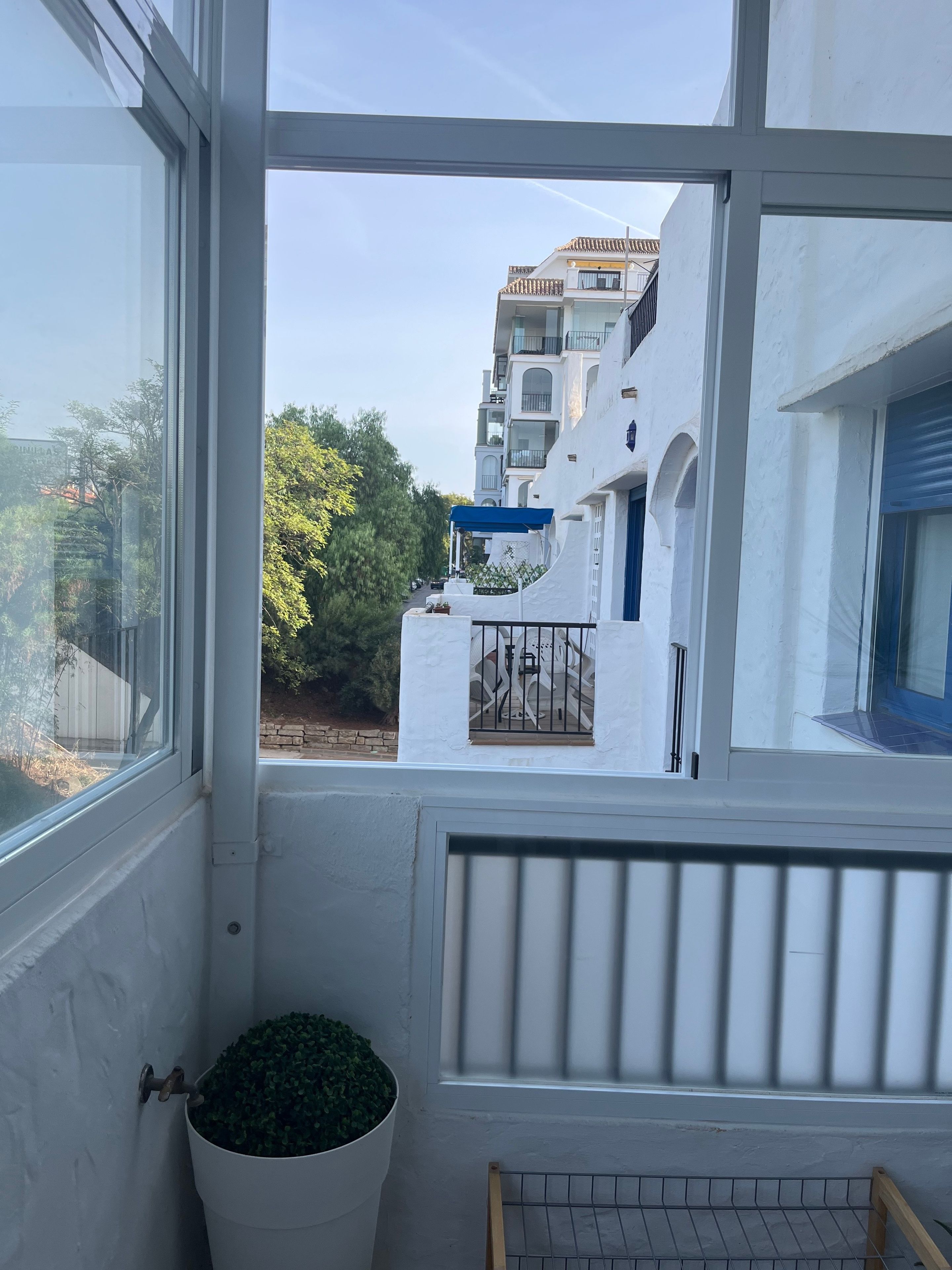 Un balcón con vistas a un edificio blanco con balcones, una planta en maceta y una barandilla de metal.