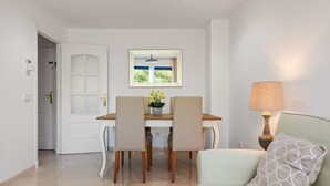 A dining area with a table and chairs, a window with a view, a lamp, and a sofa.