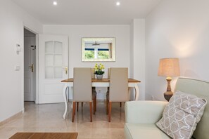 A dining area with a table and chairs, a window with a view, a lamp, and a sofa.