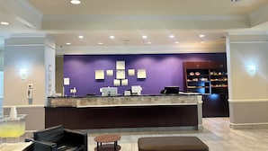 A reception area with a purple wall, a counter with a computer, and a food display. - Stay Express Inn & Suites - Mobile AL (Mobile)