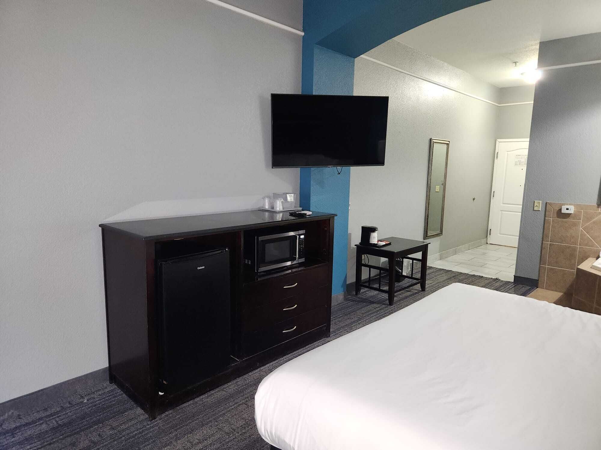 Habitación de hotel con cama, minibar, televisor montado en la pared y una mesita con cafetera.
