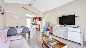 A modern living room with a sofa, dining table, chairs, a TV, and a kitchen in the background. - Maison Escapades Marines – Terrace and Comfort in the Heart of the Village (Arès)