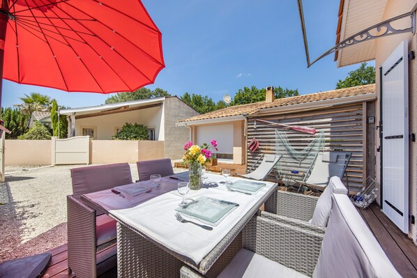 An outdoor patio with wicker furniture, a table set for dining, and a red umbrella.