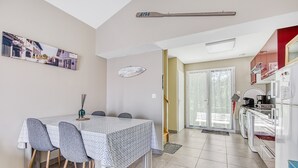 A dining area with a table and chairs, a kitchen with appliances, and a sliding glass door leading to an outdoor area. - Maison Escapades Marines – Terrace and Comfort in the Heart of the Village (Arès)