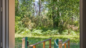 A window view of a forested area with a wooden bench and a fence. - Maison Escapades Marines – Terrace and Comfort in the Heart of the Village (Arès)