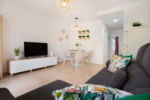 Uma sala de estar moderna com televisão de tela plana, uma área de jantar com cadeiras, um sofá com almofada floral e um lustre.