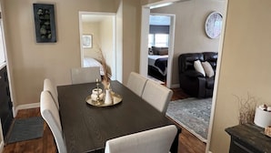 A dining area with a dark wooden table, white chairs, and a decorative vase. There is a clock on the wall and a sofa in the adjacent living room. - Sturgis Rally perfect location! (Sturgis)