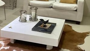 Ein Wohnzimmer mit einem weißen Sofa, zwei goldenen Kissen, einem weißen Couchtisch mit Kerzen und einem Buch sowie einem Cowhide-Teppich.