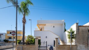 Un edificio moderno con fachada blanca, una entrada protegida por una verja y una palmera al frente.