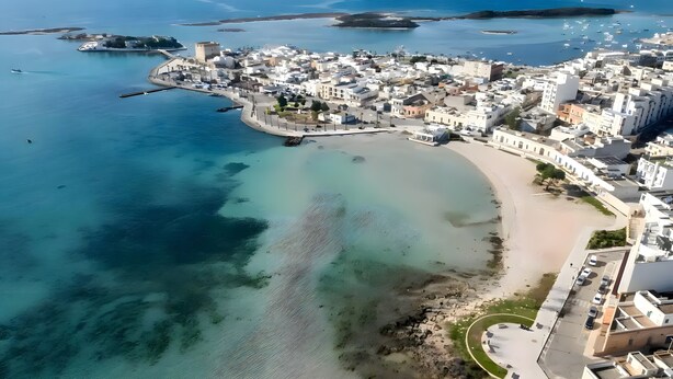Vista aérea de un pueblo costero con playa, aguas cristalinas y barcos.