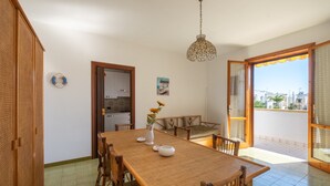 Un comedor con una mesa y sillas de madera, una lámpara colgante y vistas al exterior a través de un vidrio.