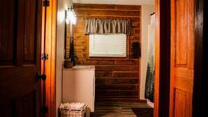 A narrow hallway with wooden walls, a window with blinds, a refrigerator, and a basket of towels.