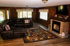 A log cabin interior with a leather sofa, a fireplace, a flat-screen TV, and a patterned rug.