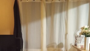 Une pièce avec un rideau blanc, une petite table sur laquelle est posé un vase de fleurs et une chaise.