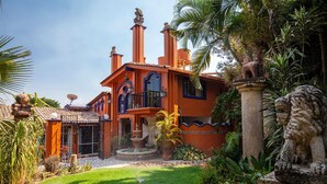 Una casa grande y ornamentada con múltiples chimeneas, una fuente y un jardín bien cuidado con plantas tropicales.