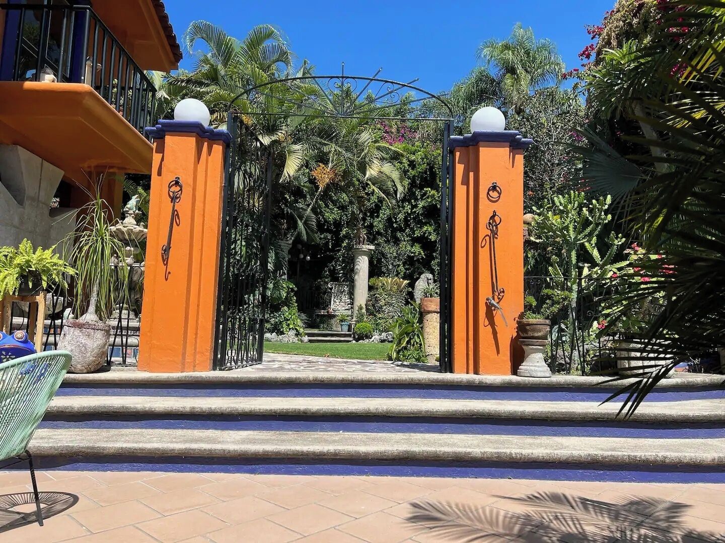 A gated entrance with steps leading to a pool area, surrounded by lush greenery and palm trees.