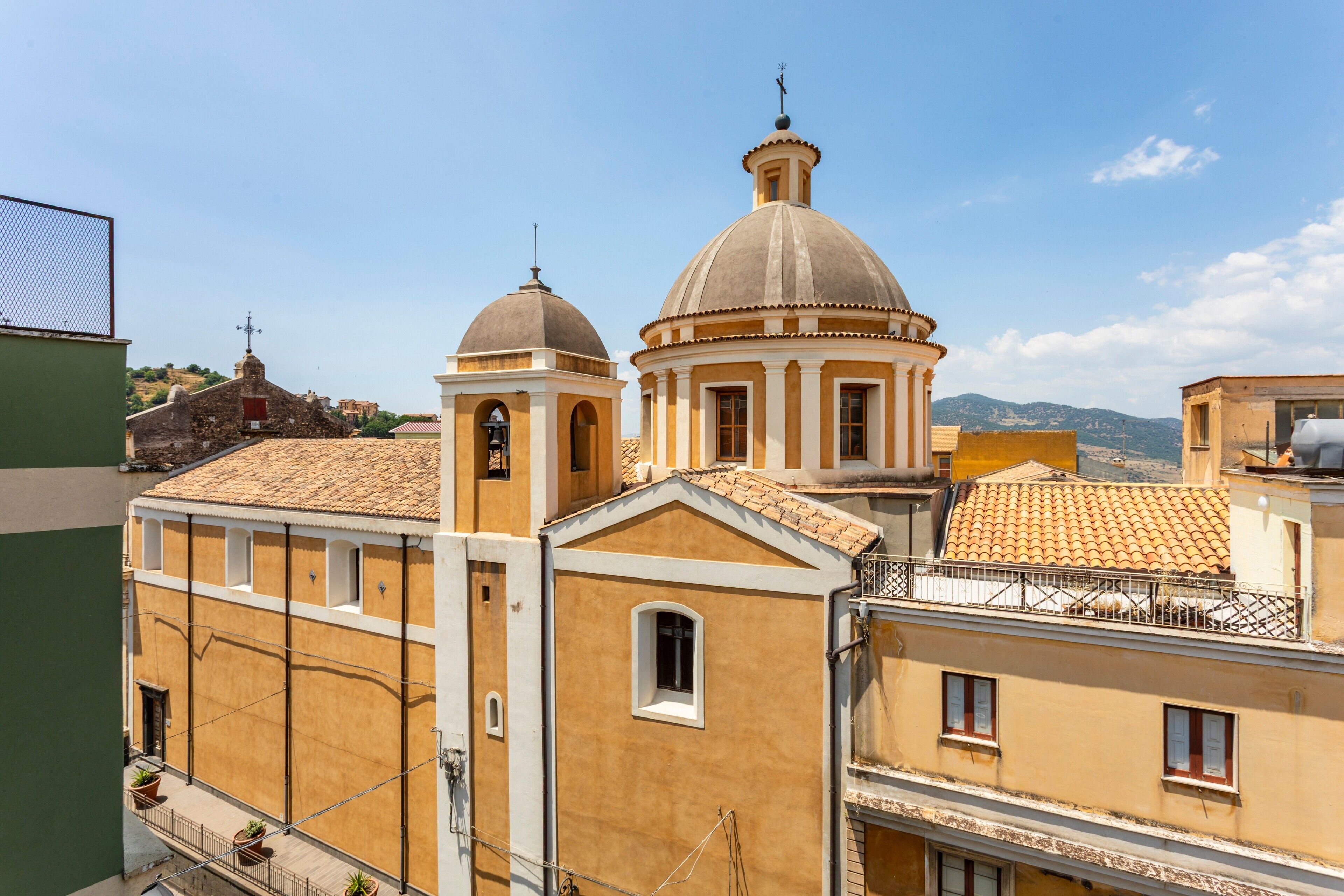 A building with a dome and bell tower, a balcony with potted plants, and a view of the surrounding area.