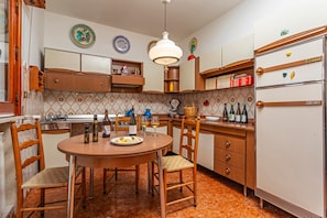 Una cocina con armarios de madera, una mesa redonda para comer, sillas, un refrigerador y varios utensilios de cocina.