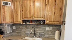 A kitchen with wooden cabinets, a granite countertop, a stainless steel dishwasher, and a built-in vent. - Pet friendly cabin in the woods perfect for your adventures (Big Bear)