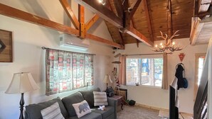 A cozy living room with a wooden ceiling, a sofa, a television, and a patterned rug. - Pet friendly cabin in the woods perfect for your adventures (Big Bear)