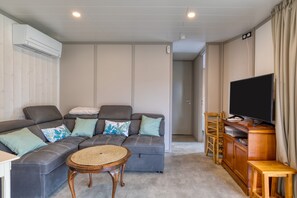 Een woonkamer met een hoekbank, een televisie, een houten kast en een geweven salontafel.