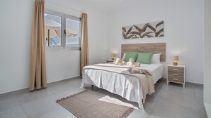 A bedroom with a bed, bedside tables, a nightstand, a window with curtains, and a wall-mounted artwork. - Holiday Home 'Gara Fuerteventura' with Pool, Wi-Fi and Air Conditioning (Gran tarajal)