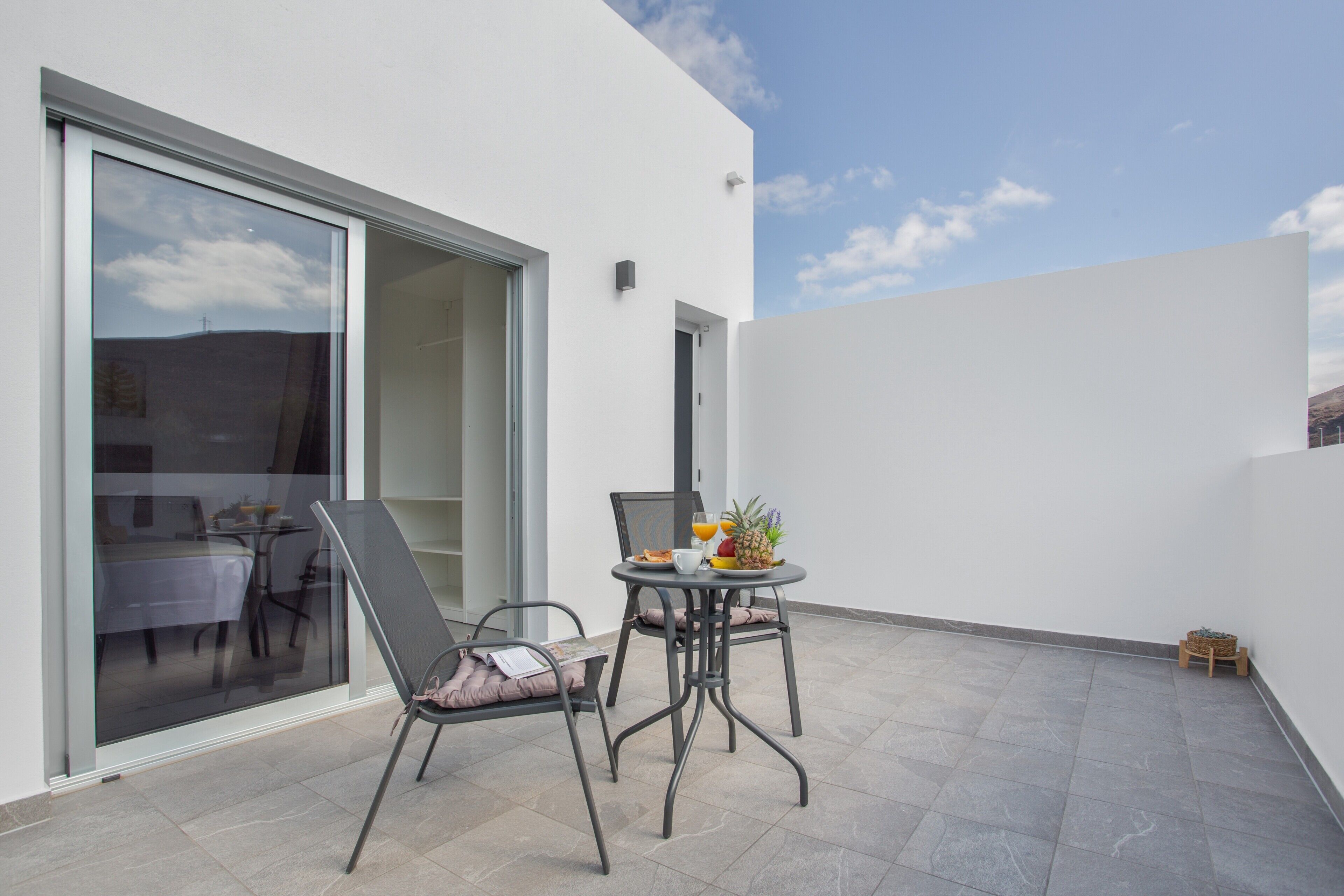 Une terrasse extérieure moderne, avec une table dressée pour le petit-déjeuner, une chaise et une porte-fenêtre coulissante donnant sur un espace de repas intérieur.